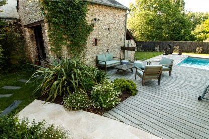 Une terrasse en bois avec un salon d ejardin et une piscine dans le fond